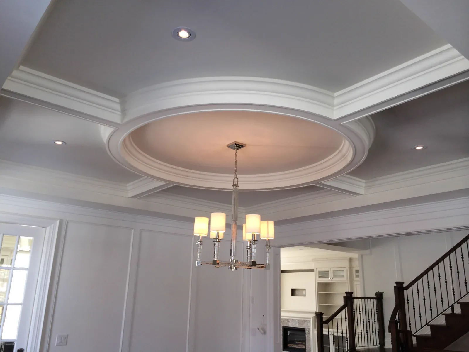 Concentric ceiling curves and coves turn a circular recess into a focal point, with a chandelier anchoring the room below.